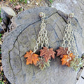 Polymer clay autumn leaf earrings with orange, mauve, and green charms dangling from silver-tone chains and stud tops