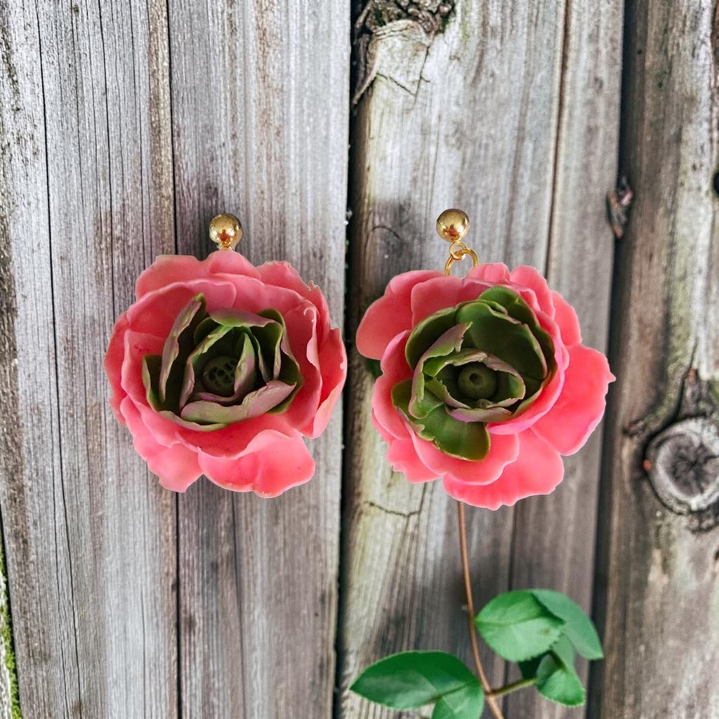 Pink rose polymer clay flower earrings with gold stud posts against a rustic wood background